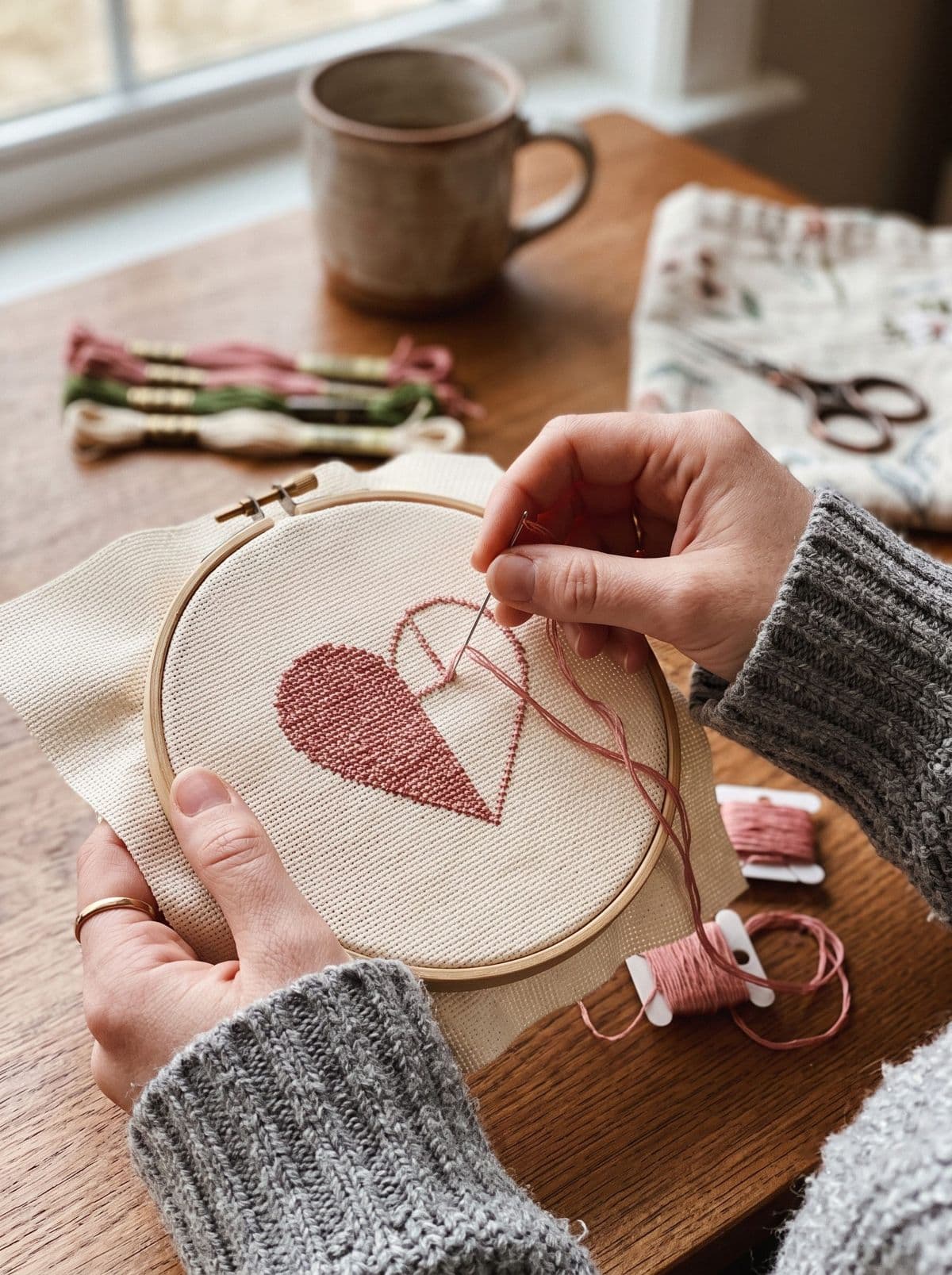 Half-finished dusty rose cross stitch heart in a hoop